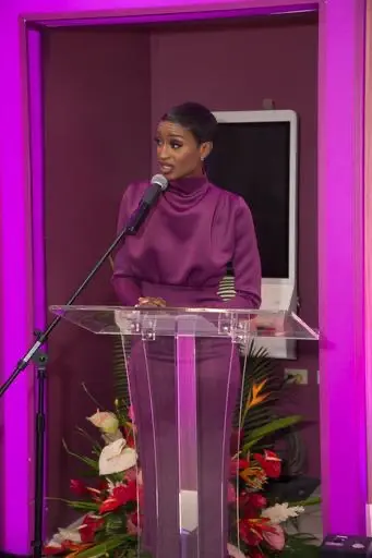 Ainka Will presenting at a podium in a purple dress