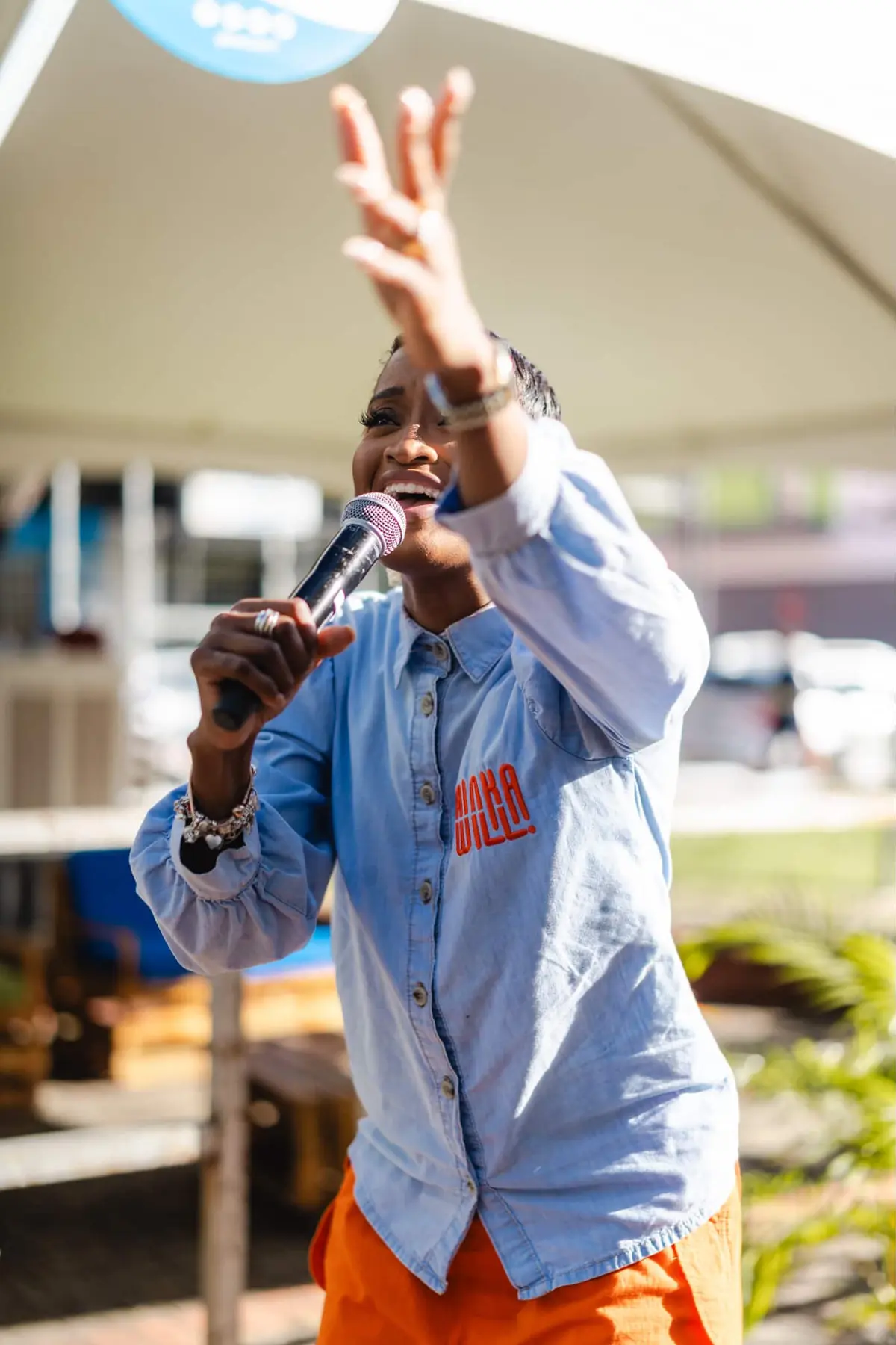 Ainka Will speaking with her arm raised at an outdoor event