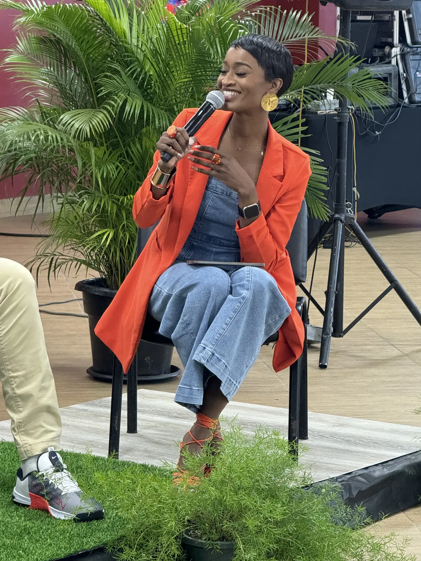 Ainka Will seated in an orange blazer moderating an outdoor session