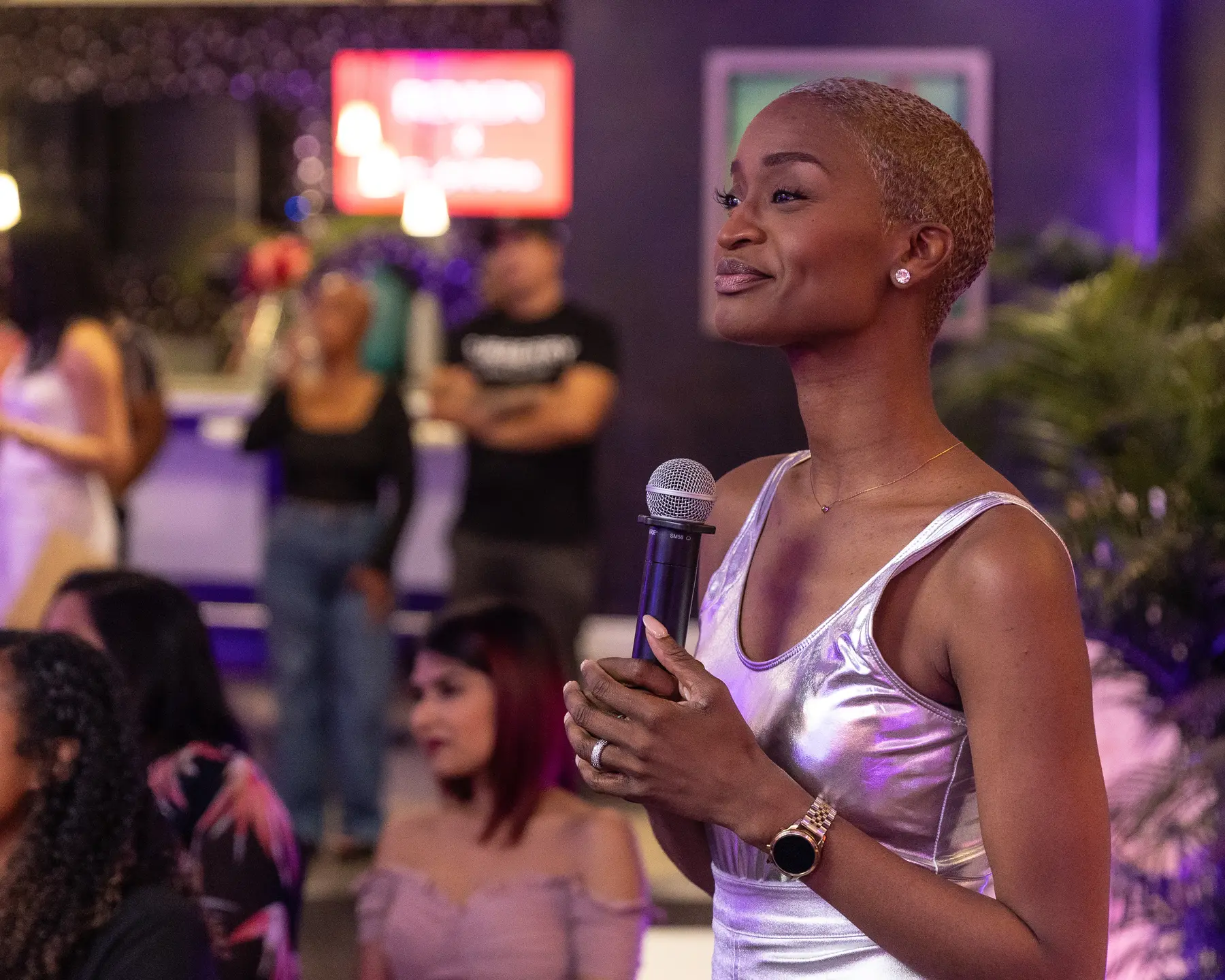 Ainka Will with a microphone in a silver top at Bocas Lit Fest